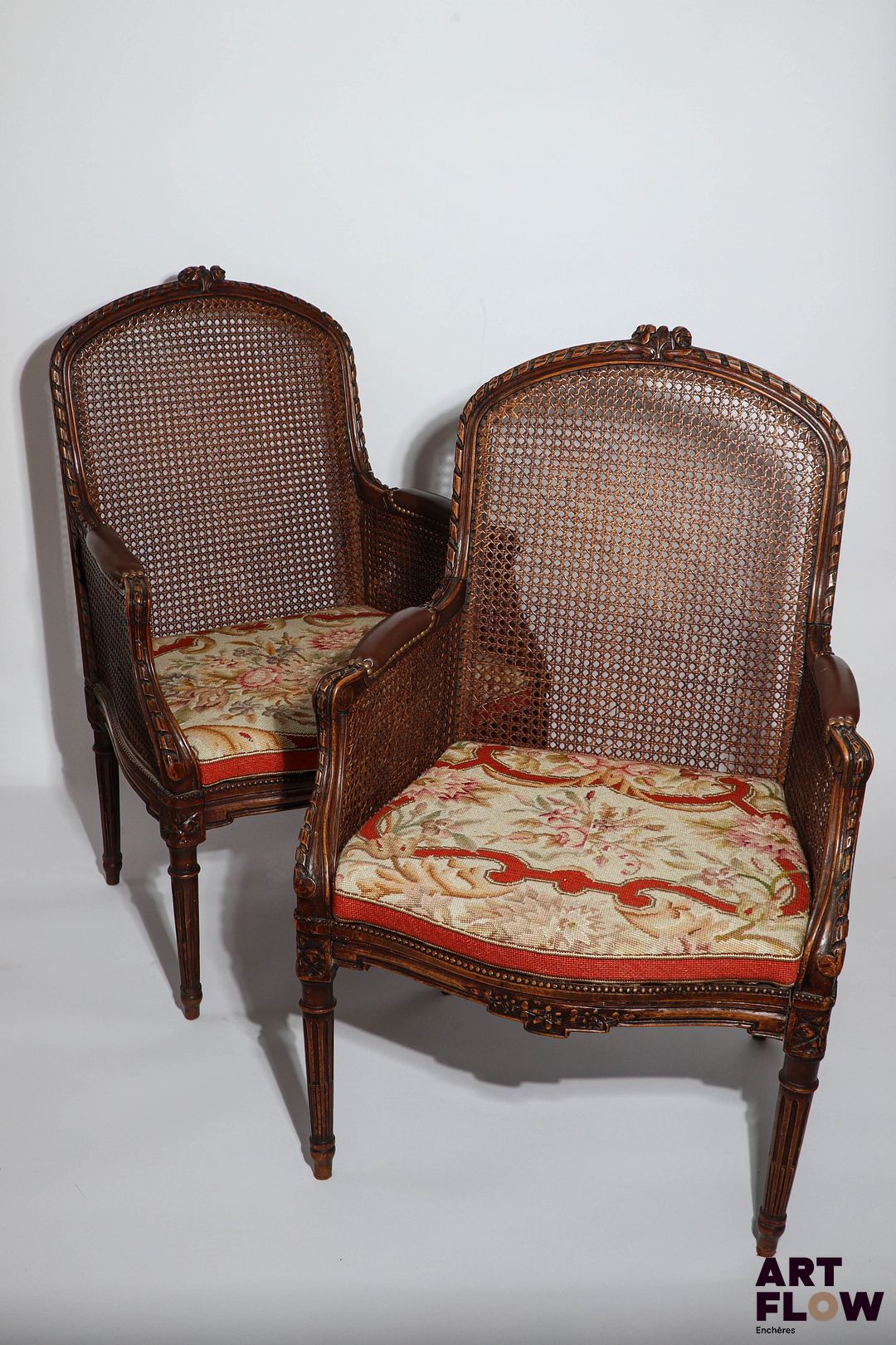 Paire de larges bergères cannées en bois mouluré et sculpté, accotoirs à manchette. Garnies d'un carreau amovible de tapisserie au petit point. De style Transition. 99 x 64 x 45 cm. Accidents et restaurations.