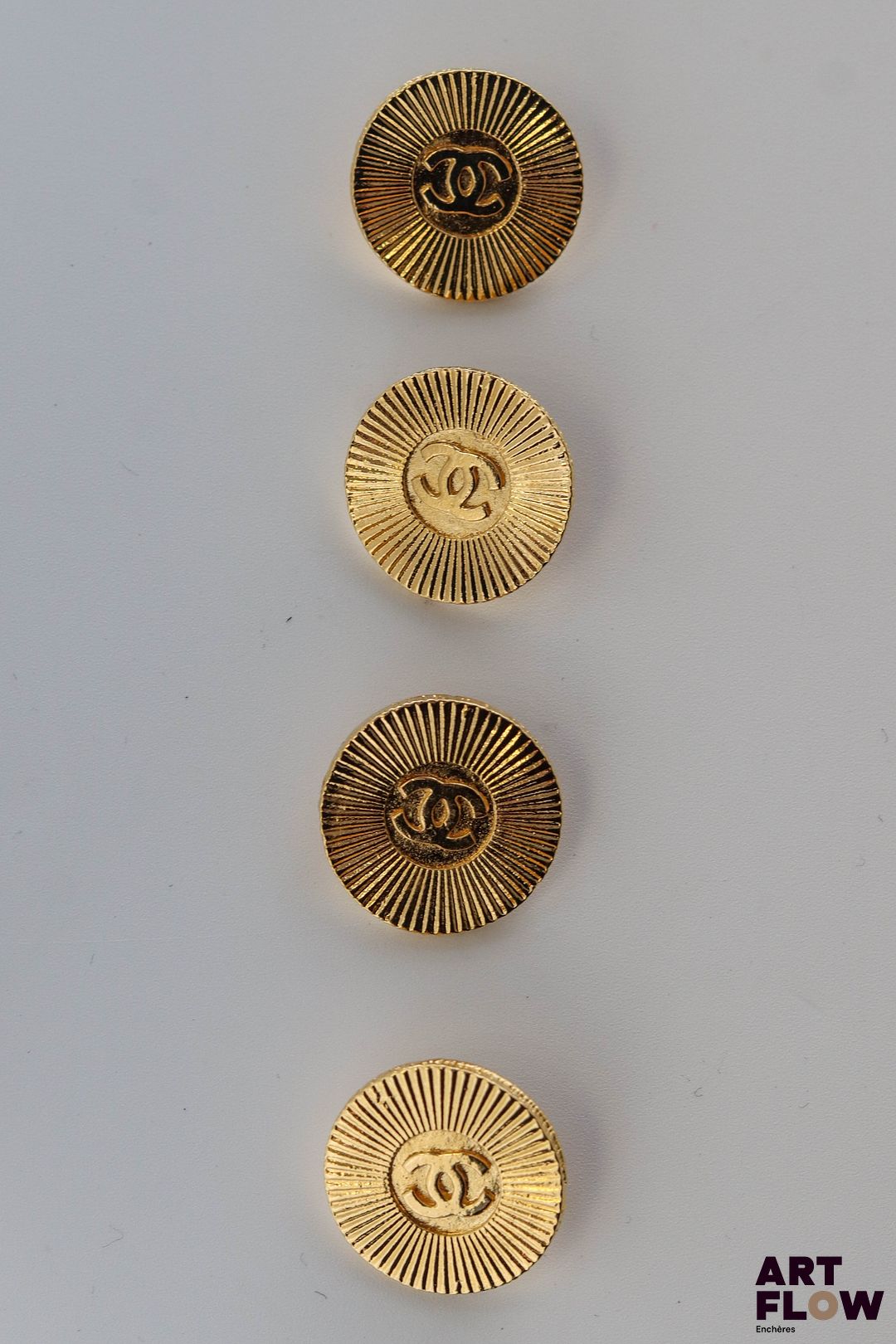 CHANEL Lot de 4 boutons en métal doré à décor guilloché rayonnant et sigle Chanel.