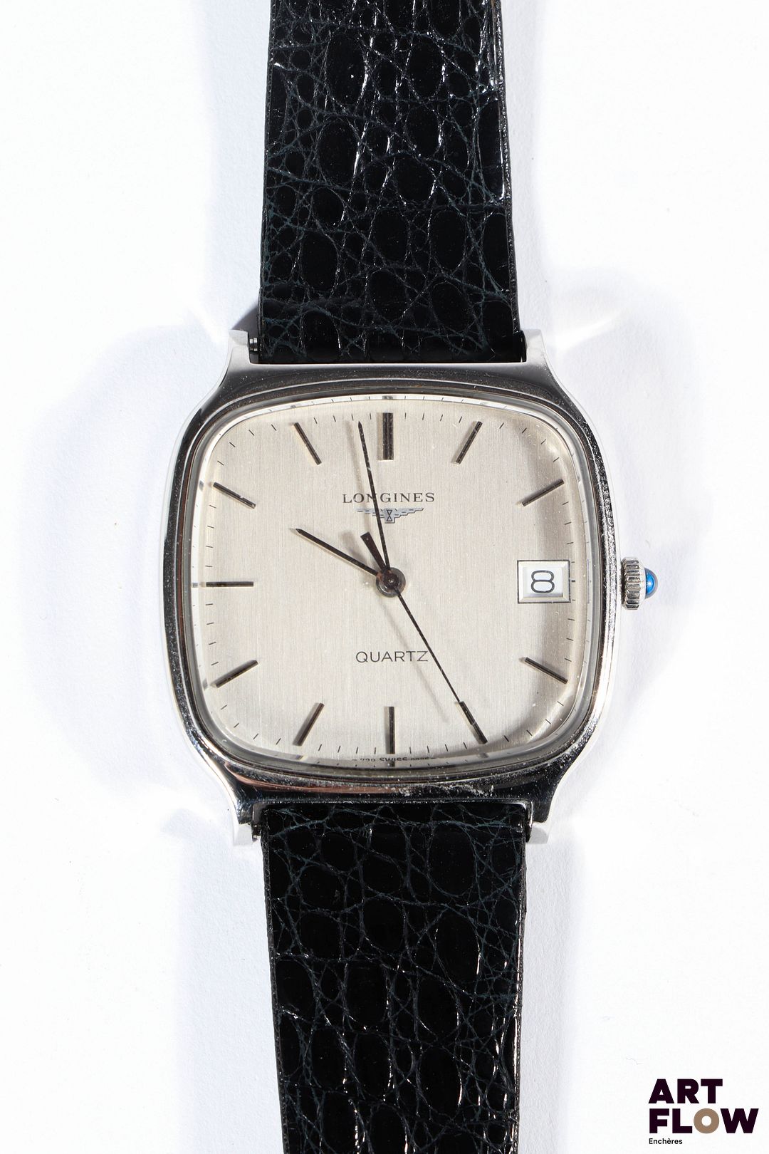 LONGINES Montre bracelet homme en acier, à mouvement à quartz, le boîtier de format Tv screen à cadran à fond brossé argenté, index bâton, guichet date à 3h, lunette lisse, cabochon en pierre synthétique bleu, le bracelet en cuir d'origine. Années 1970 33 x 31 mm Longueur du bracelet : 17 cm env. Longines, fondée en 1832 à Saint-Imier, est une maison suisse emblématique réputée pour sa précision chronométrique et son élégance intemporelle, notamment dans l’aviation et le sport. Très légères rayures d'usage. Non fonctionnelle au moment de la rédaction du catalogue, pile à changer.