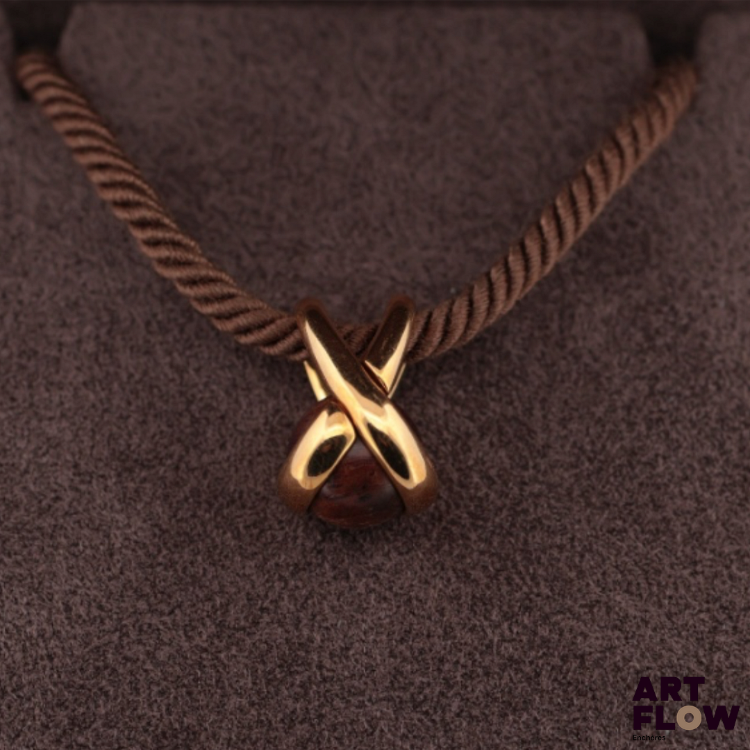 CHAUMET Pendentif en or jaune en forme de lien croisé, serti d’une boule de bois précieux, coulissant sur une cordelette de coton, les extrémités en argent. Le pendentif signé « Chaumet Paris » et numéroté 329787. Dans son écrin, état parfait du pendentif et du cordon. Poids du pendentif : 4.67 g