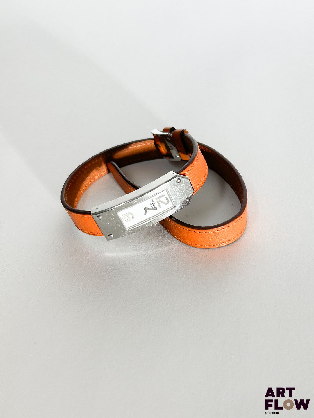 HERMÈS Modèle Kelly II Référence : KT1.210 Montre bracelet de dame à boitier en acier vissé, signé et numéroté, cadran à fond blanc à deux index chiffres arabes appliqués, montée sur un bracelet double tour en cuir orange à boucle ardillon signée Hermès. Mouvement quartz. Diamètre boitier : 15 x 41 mm Longueur : 36 cm environ Bracelet rapporté Avec facture