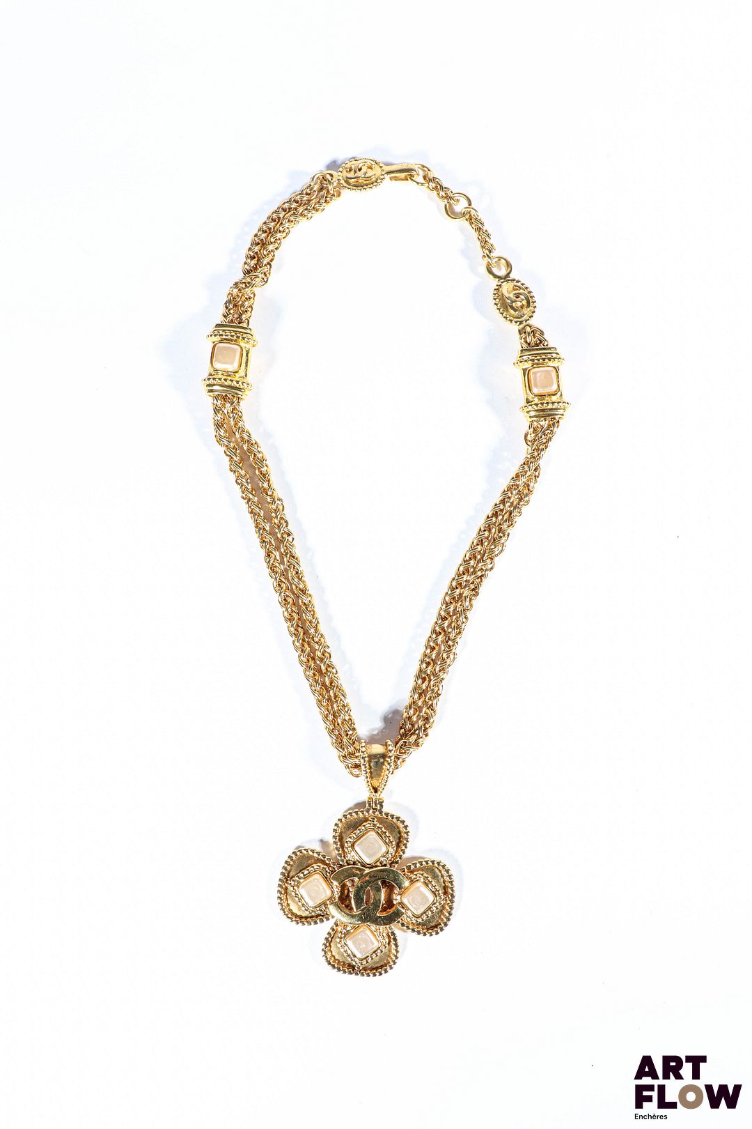CHANEL - GRIPOIX Collection Automne/Hiver 1996 Collier en métal doré orné d'un pendentif formant un trèfle décoré de cabochons en pâte de verre nacrée et monogrammé Chanel au centre Chaines entrecoupées de motifs carrés ornés de pierres en pâte de verre du même coloris Fermoir décoré du logo Chanel, et inscription sur la plaque "96 A" La Maison Gripoix, fondée à Paris à la fin du XIXᵉ siècle, est célèbre pour sa technique artisanale de pâte de verre imitant les pierres précieuses. Gabrielle Chanel va ainsi collaborer étroitement avec Gripoix pour créer des bijoux audacieux mêlant inspiration antique et modernité. Longueur : 48 cm Très bon état général. Infimes rayures d'usage.