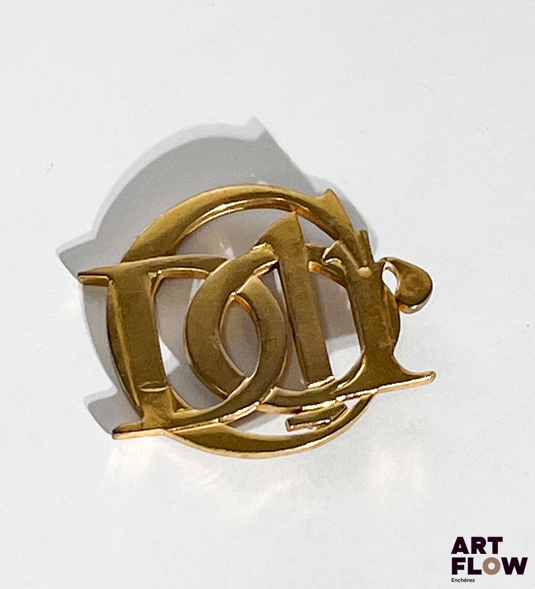 PARFUMS CHRISTIAN DIOR Broche en métal doré, signée au dos. Dimensions : H. 5 x L. 6 cm On y joint deux pins Dior