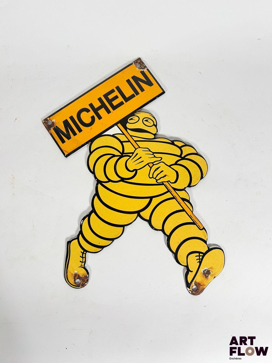 Plaque émaillée Michelin représentant le bonhomme Michelin portant une pancarte Dimensions : 28 x 22 cm Petits éclats et traces de rouille Reproduction moderne