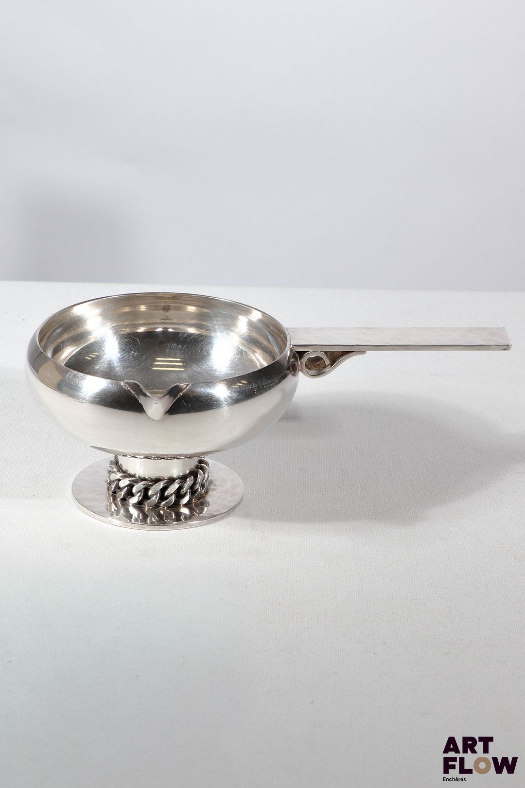 Jean DESPRES (1889-1980) Coupe vide poche ronde sur piédouche en métal argenté évoquant un poêlon. La base soulignée d'une chaine. Signée J. DESPRES à la pointe au revers de la prise et datée 6/7/68 sous la base. Haut. : 7,5 cm L. : 21,5 cm Dans sa boite d'origine Rayures d'usage