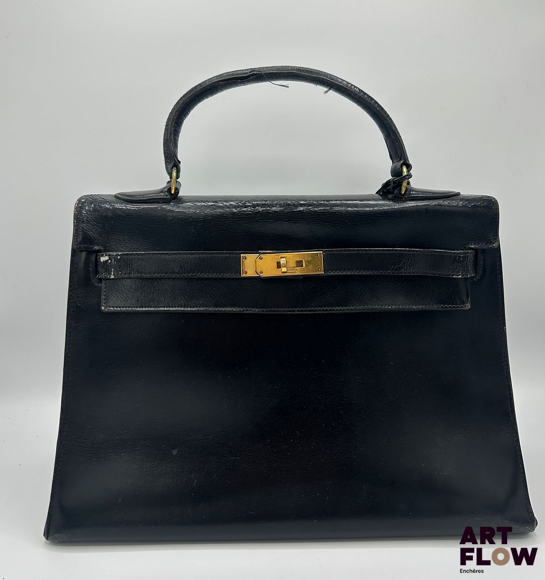 HERMÈS Paris Circa 1950 Sac à main Kelly en cuir box noir, garnitures en métal doré, avec cadenas et clochette avec clés. Intérieur à une poche plaquée double à l'avant et une poche plaquée simple à l'arrière du sac. H : 25 x L : 32 x P : 13 cm Usures, défauts d'usage, craquelures, griffures et frottements Dustbag