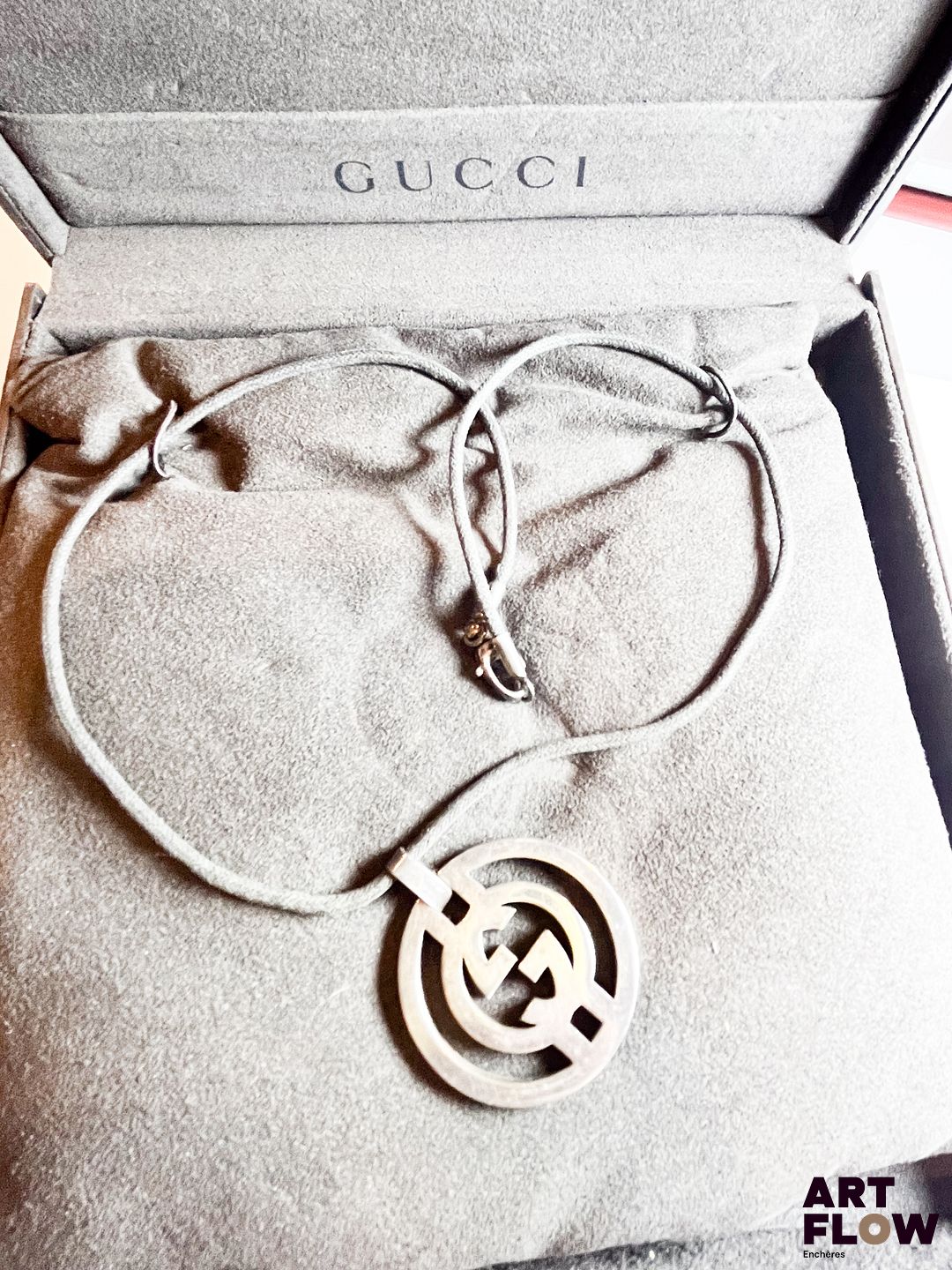 GUCCI Collier pendentif en argent 925/°° de forme circulaire, ajouré figurant le logo de la marque, sur un cordon textile Poids brut : 21,08 gr En l'état Dans son écrin