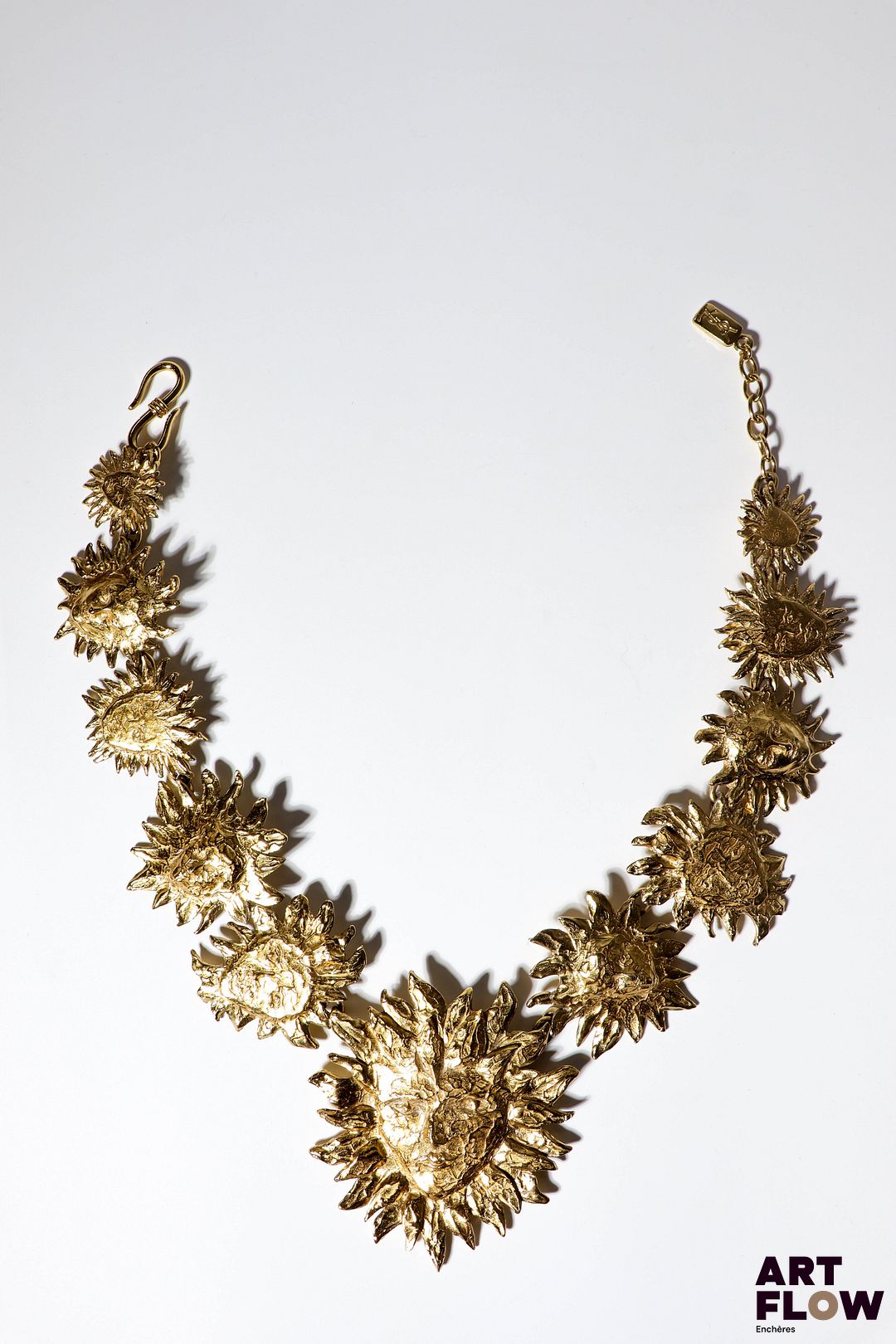 YVES SAINT LAURENT x Goossens Collier en métal doré à décor de soleils. L. 50 cm env. Très légère dédorure sur les anneaux. Modèle rare : sont surtout connus les colliers avec un unique soleil fixé sur collier torque. Le nôtre présente 10 soleils de formes différentes et aux visages plus ou moins esquissés, encadrant un soleil central imposant. Provenance : collection de la famille d'un ami et collaborateur de Robert Goossens.