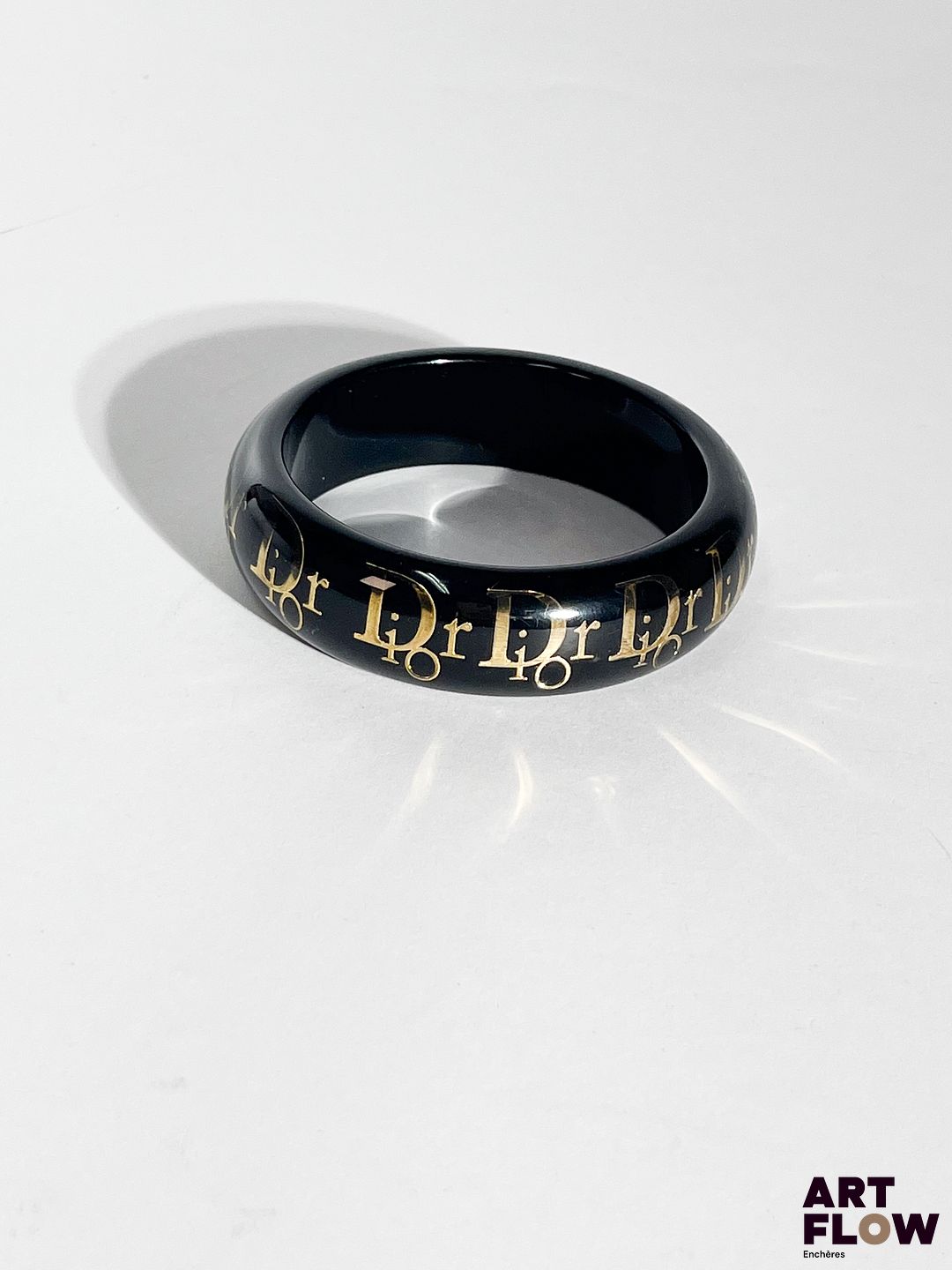 CHRISTIAN DIOR Manchette en résine transparente sur fond noir et inscription de la marque dorée. Diamètre : 8 cm