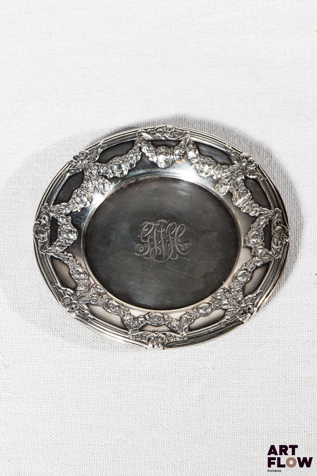 Sous verre en argent, de forme ronde à riche décor de guirlandes de fleurs et noeuds, le centre chiffré. Poids brut : 30 g Diamètre : 9 cm