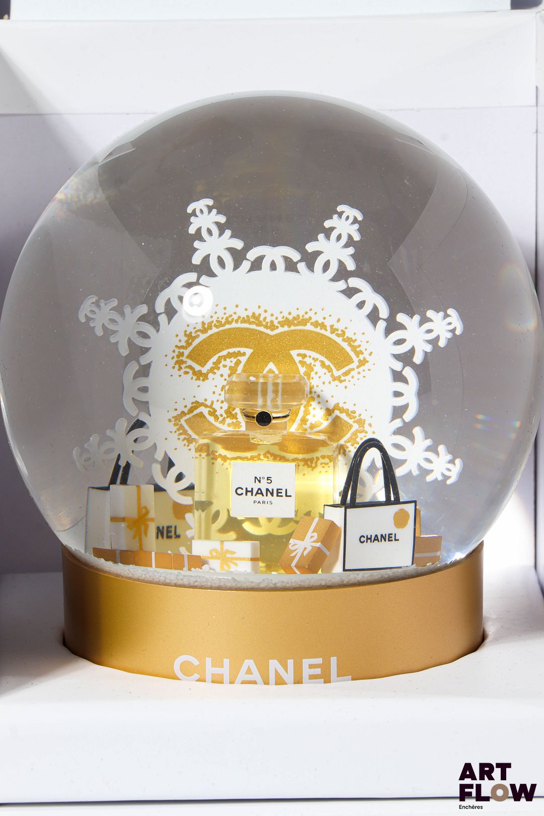 CHANEL Beauté Boule à neige figurant un flocon derrière un flacon de parfum « N°5 » entouré de paquets cadeaux. Signée. H. 12 cm Edition limitée Dans sa boîte d’origine Etat neuf