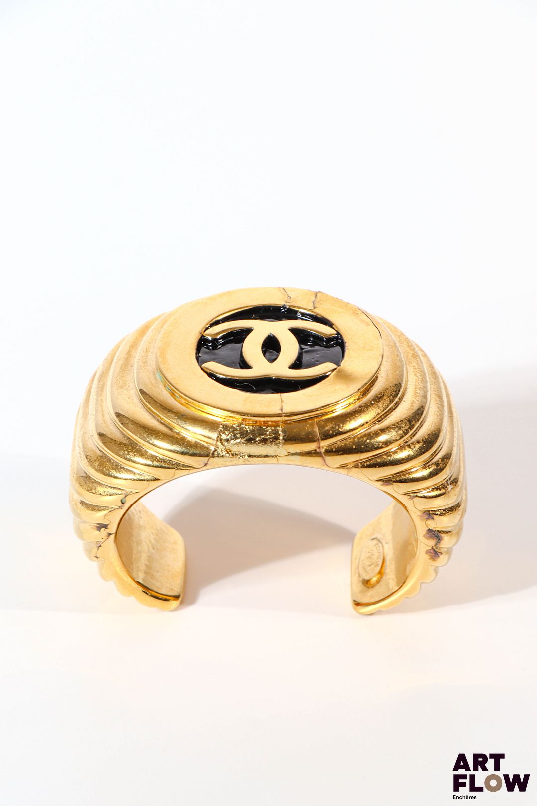 CHANEL Bracelet jonc en métal doré avec le double C sur fond noir en son centre. Diamètre : 5,5 cm environ Usures à la dorure