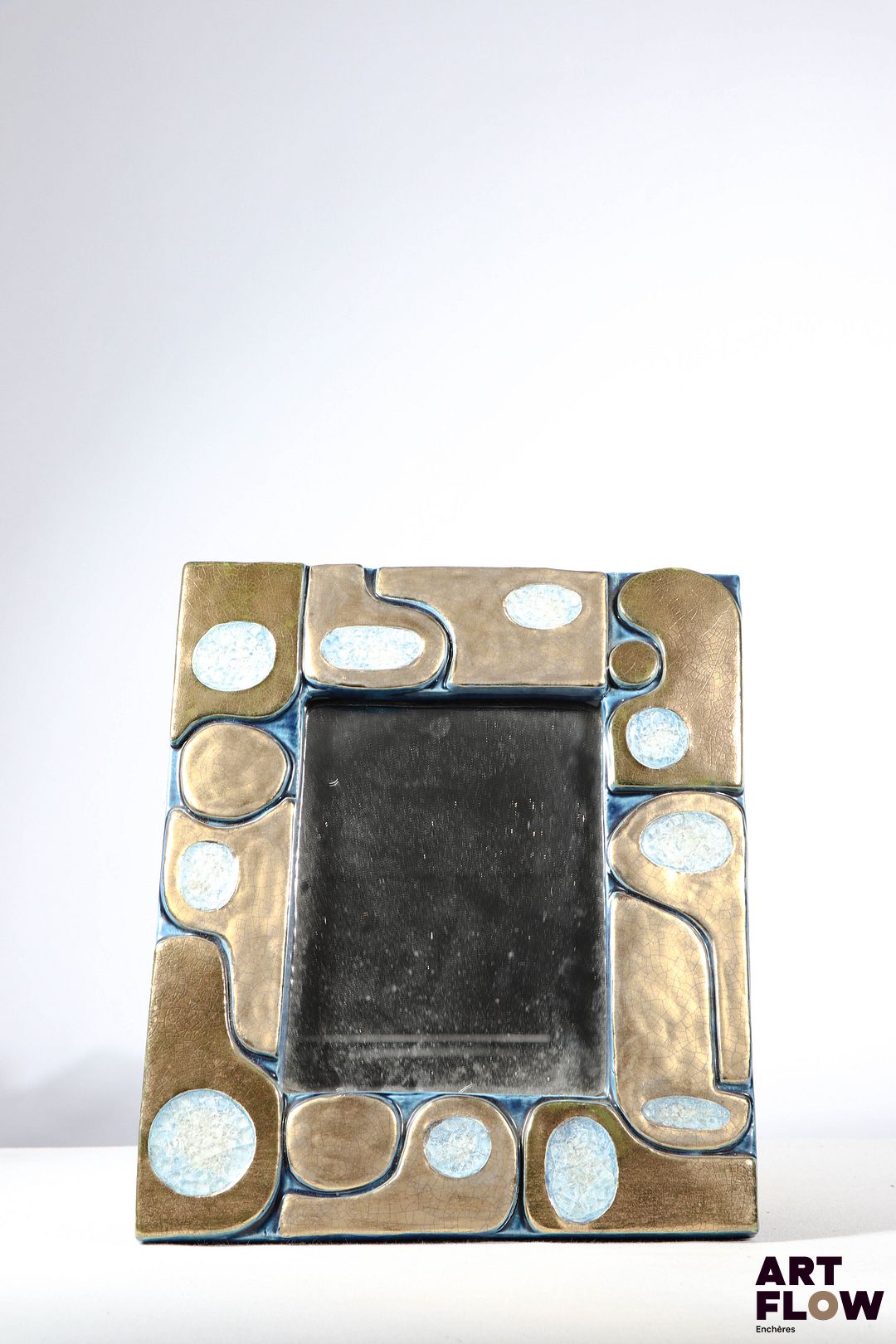 Mithé ESPELT (1923-2020) Miroir Ouvéa en céramique émaillée bleu et doré. Les parties dorées et celles en pâte de verre craquelées. Le dos gainé de feutrine verte. Dimensions : 31,5 x 27 cm Bon état général malgré quelques légers défauts (petites usures d'usage de l'émail).