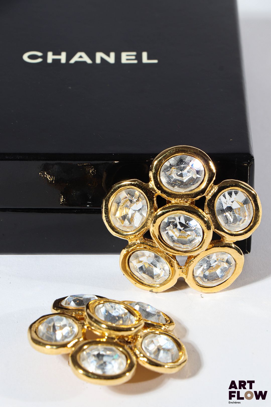 CHANEL Paire de clips d'oreilles en métal doré formant des fleurs stylisées ornées de strass. Dimensions : 4,5 cm environ Dans leur boîte d'origine.