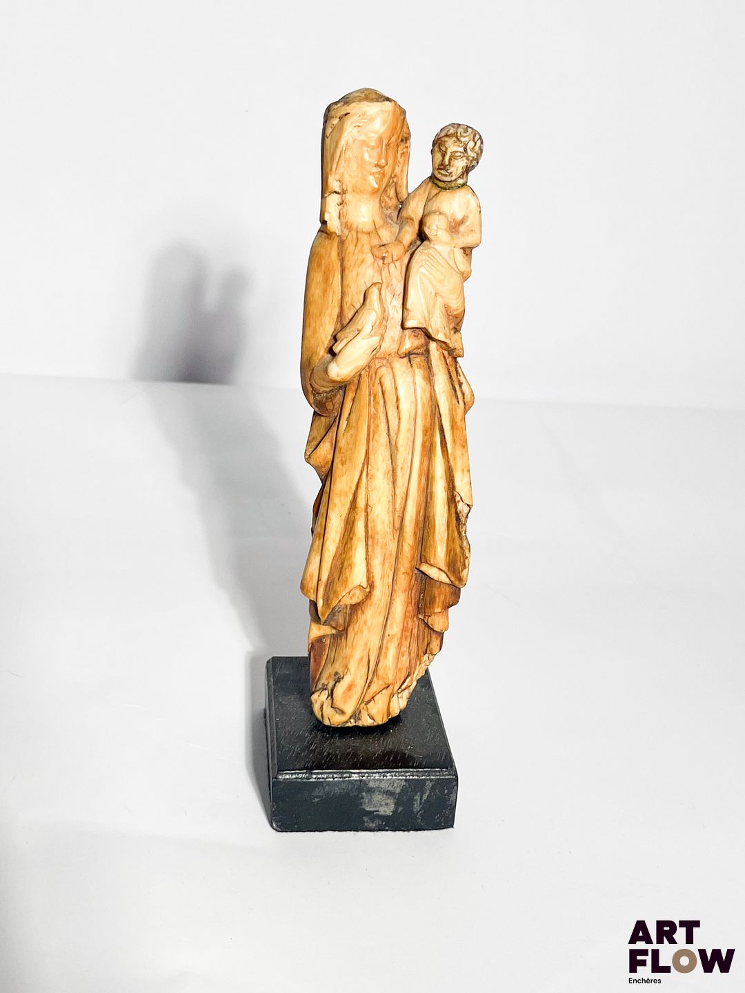 Vierge à l’Enfant en ivoire sculpté en ronde-bosse. Debout, la Vierge tient une colombe dans sa main droite et porte son Fils sur son côté gauche ; la tête ceinte d’une couronne posée sur un voile, elle est vêtue d’une longue robe ceinturée et d’un manteau ouvert dont les pans sont retenus par les avant-bras ; l’Enfant pose sa main droite sur la poitrine de sa Mère et tient l’orbe de l’autre. Fin du XIVe siècle Hauteur : 19 cm Socle en bois noirci (petits accidents, tête de l’Enfant d’époque postérieure) Conformément à la règlementation en vigueur, ce lot sera délivré avec son certificat Intra Communautaire (FR2401300105-K) Provenance : Vente aux enchères du 16 mars 2016, Thierry de Maigret, lot 13 Expertise : Cabinet Fligny