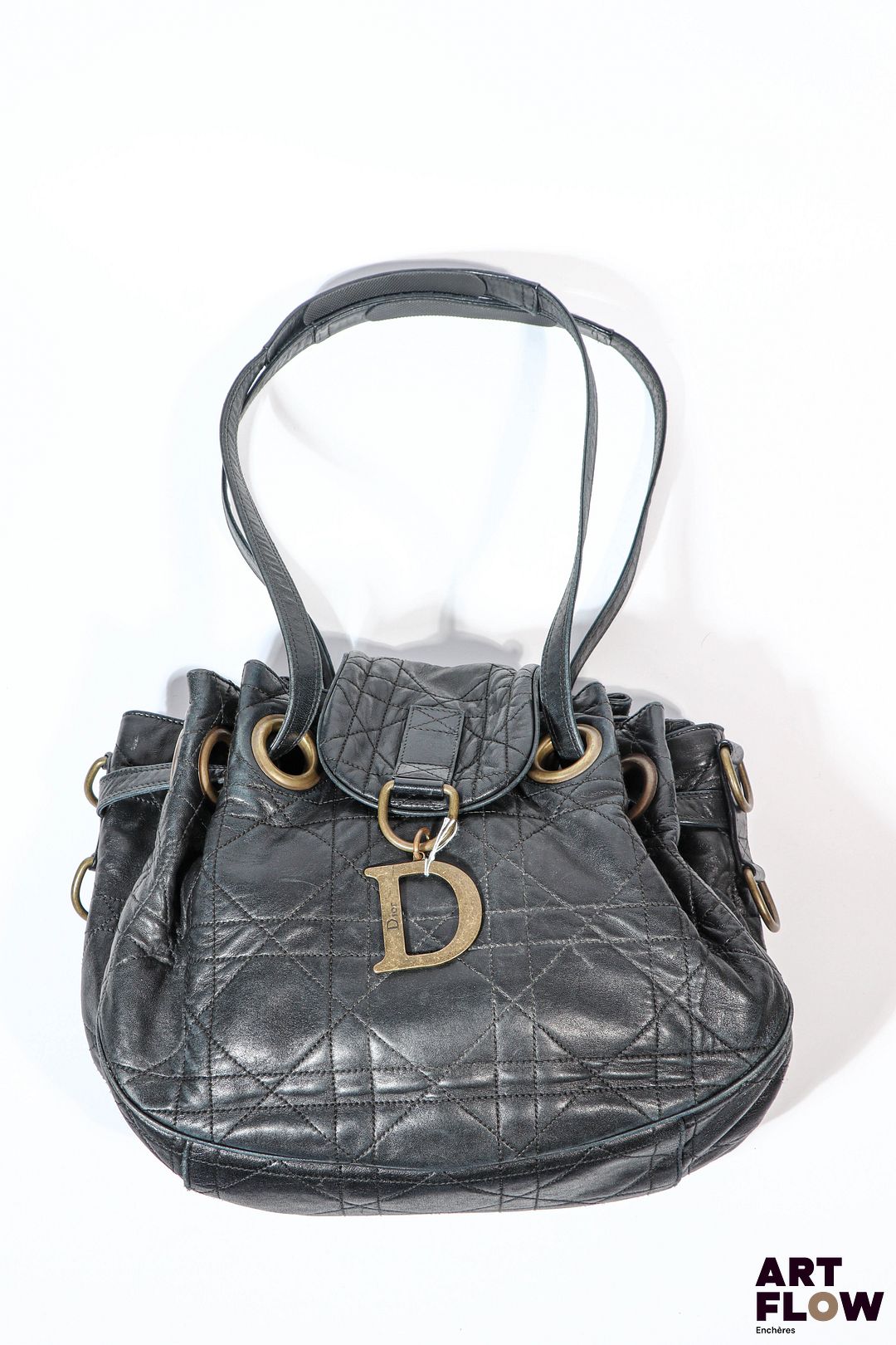 CHRISTIAN DIOR 2008 Sac modèle Drawstring en agneau noir surpiqure motif cannage, orné d'un D en métal patiné vieux or. Anse formant cordon de serrage en cuir, anneaux et bijouterie également en métal patiné vieux or. Doublure en tissu satiné rouge monogrammé avec deux poches plaquées et une poche zippée. 35 x 25 x 17 cm Bon état général malgré quelques défauts (usures d'usage, taches à l'interieur)