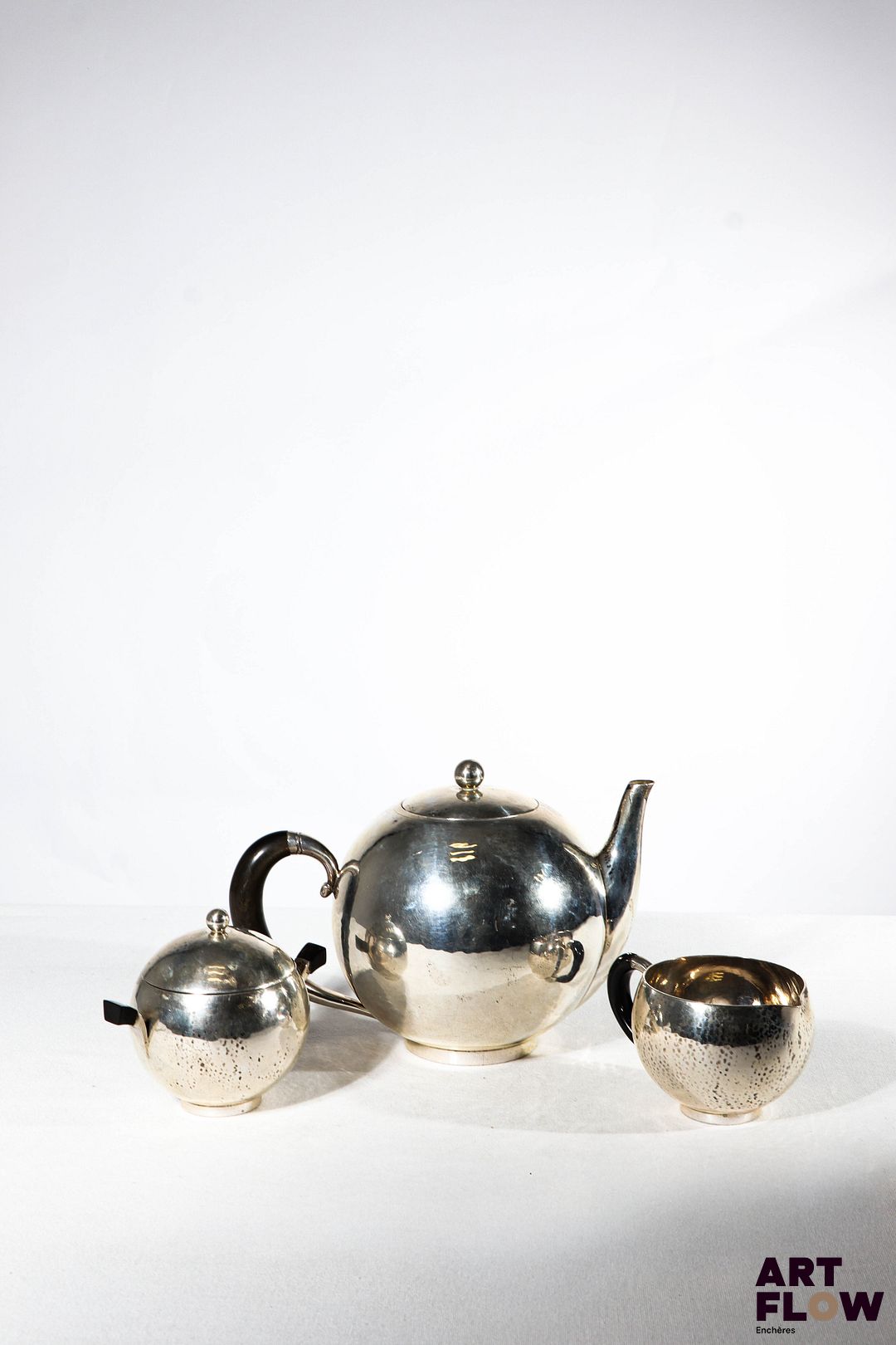 GEORG JENSEN Service à thé en argent comprenant une théière, un sucrier et un pot à lait, en métal délicatement martelé. Poinçons Gorg JENSEN, Danmark. Théière : H. 15 cm x D. 21 cm environ Sucrier : H.9,5 cm x D 12 cm environ Pot à lait : H. 6 cm x D. 11, 5 cm environ Poids brut : 843,68 g