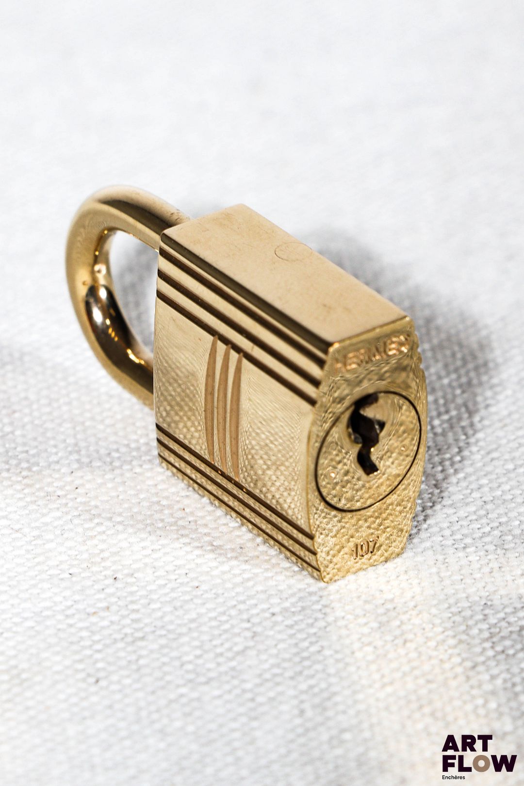 HERMÈS Cadenas en métal doré gravé d'un H n°107 avec ses deux clés 3,5 x 2 cm Très bon état général malgré quelques très légers défauts (Petites usures d'usage)
