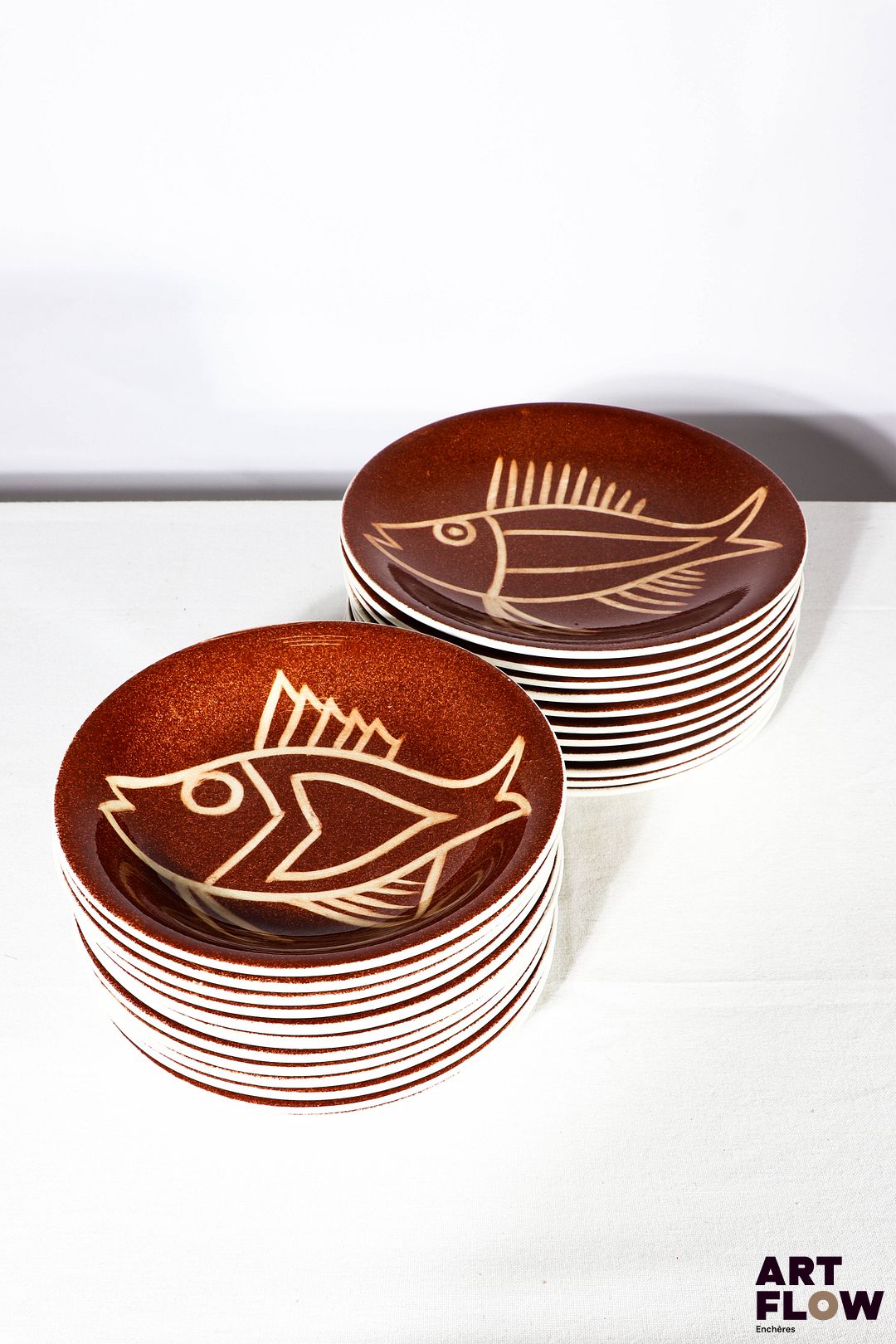 Robert PICAULT (1919-2000) - Vallauris. Importante partie de service en céramique émaillée à fond ocre, ornées d'un décor de poissons, comprenant : - 12 assiettes plates. D. 24 cm - 11 assiettes creuses. D. 20 cm. Cachet "Créations de PICAULT déposé" Très bon état général malgré quelques très légères traces d'usage (infimes sauts à la couverte sur certaines assiettes).