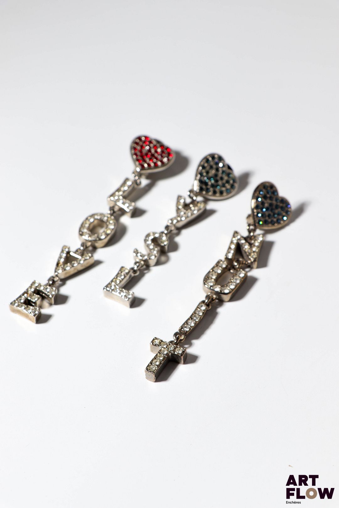 YVES SAINT LAURENT Trois clips d'oreilles ornés de coeurs retenant un lettrage en pampille LOVE/NUIT/YSL, à strass. L. 9 à 11 cm Manquent deux strass. Petites usures conformes à l'âge des pièces. Provenance : collection de la famille d'un ami et collaborateur de Robert Goossens.