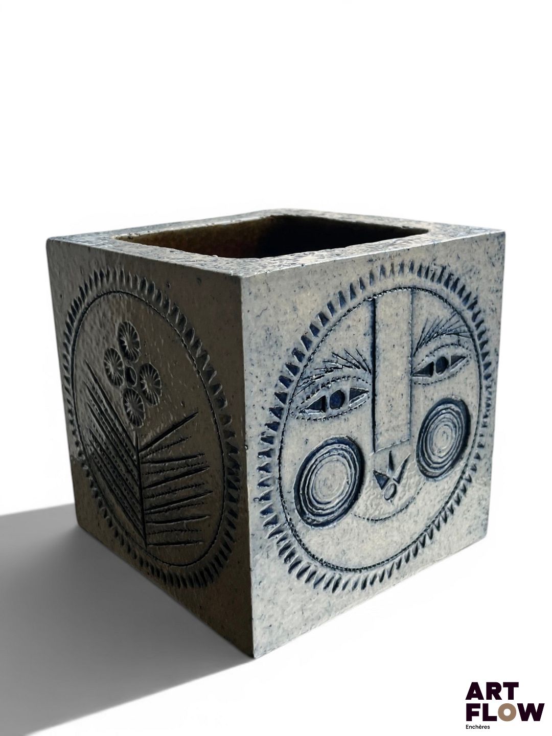 Roger CAPRON (1922-2006) Cache pot carré en grès émaillé grand feu gris bleu à décor incisé de soleil et de fleurs stylisés. Signé du cachet sous la base. H. 15 x L. 14 x P. 14 cm Eclats mineurs (base et face supérieure) Nous exprimons notre gratitude à la famille Capron pour son éclairage.