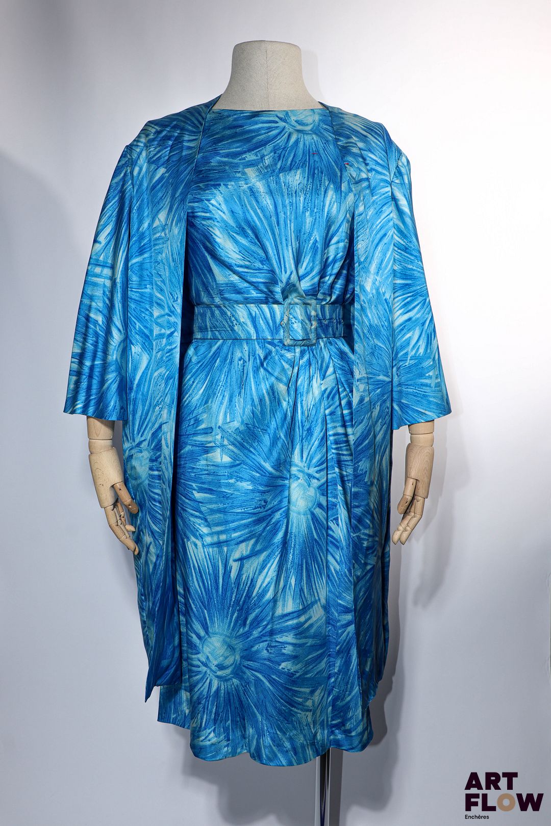 PIERRE BALMAIN Haute couture Circa 1950 Provenance : Mme Geneviève de Gaulle Anthonioz, entrée au Panthéon en 2015 Robe de cocktail en soie imprimée d'un motif floral stylisé dans les tons bleus. Elle est composée d'une robe mi-longue à manches courtes à plissé ramassé sur la taille avec sa ceinture coordonnée et d'un manteau à manches 3/4 sans boutonnage, fendu sur toute la hauteur au dos, à finition noeud plat entre les épaules. Rehaussée de la rosette de la Légion d'honneur Taille présumée 36/38 Bon état général malgré quelques défauts (petites tâches, décousue par endroit, petits fils tirés)