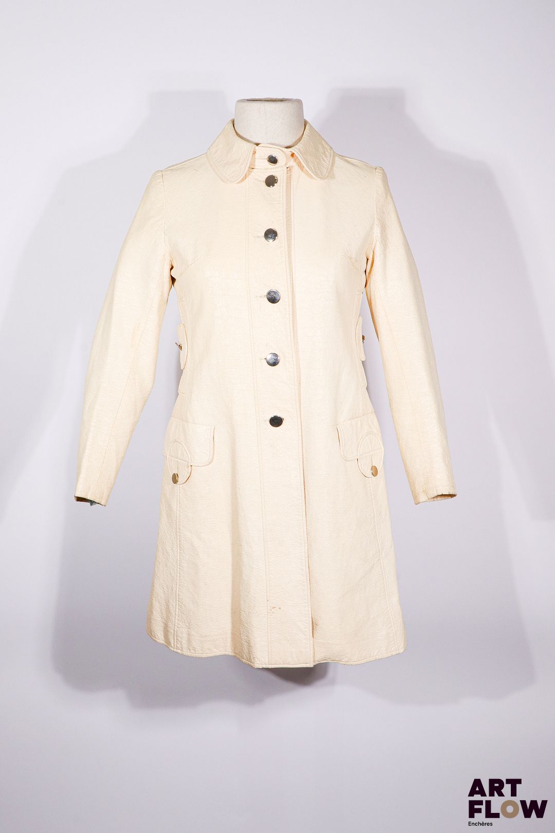 LOUIS FÉRAUD - Trench-coat "Mademoiselle Pluie Paris" - circa 1966 - Manteau 7/8 en vinyle beige, col rond, simple boutonnage, deux fausses poches verticales boutonnées, en rappel aux deux poches horizontales - Griffe noire, graphisme blanc - Taille présumée 36 - Bon état général malgré quelques défauts (craquelures)
