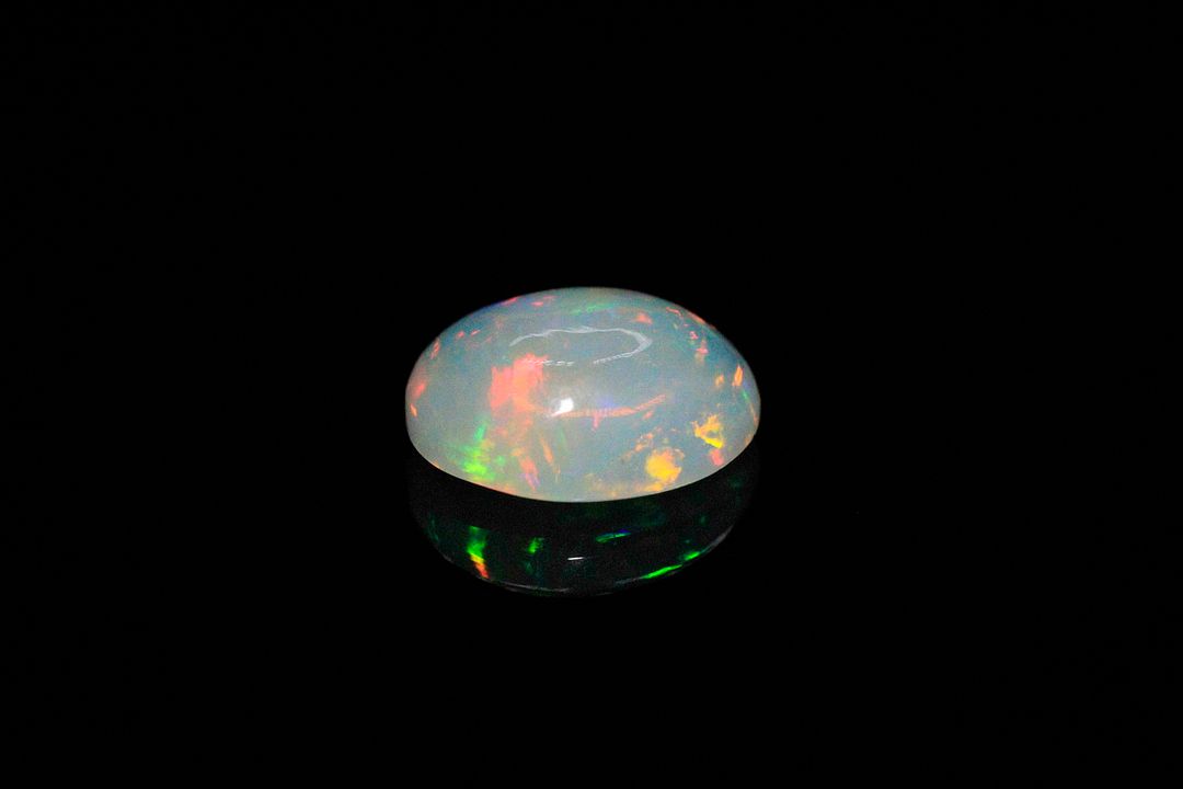 Opale blanche cabochon ovale. Beaux éclats de couleur, dominante rouge. 2.85 cts. 12.0mm x 10.0mm