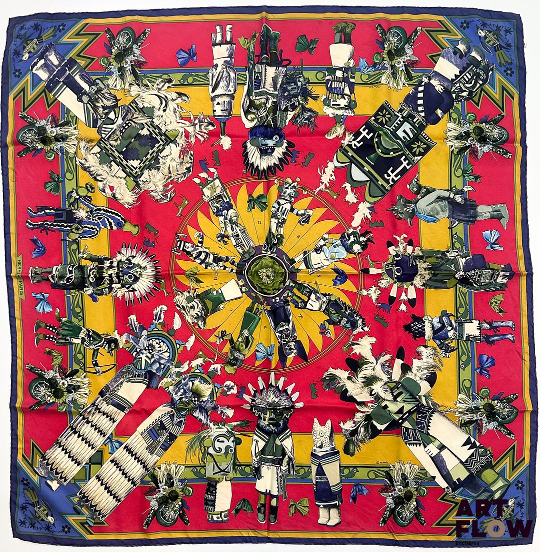 HERMÈS Modèle "Kachinas" d'après un dessin d'Oliver KERMIT Carré en twill de soie dans les tons rouges, jaunes, et bleus 90 x 90 cm Salissures. Avec boîte Bibliographie : Genevieve Fontan, Carrés d'art, Dictionnaire illustré des carrés Hermès valeur, 2025, p.149
