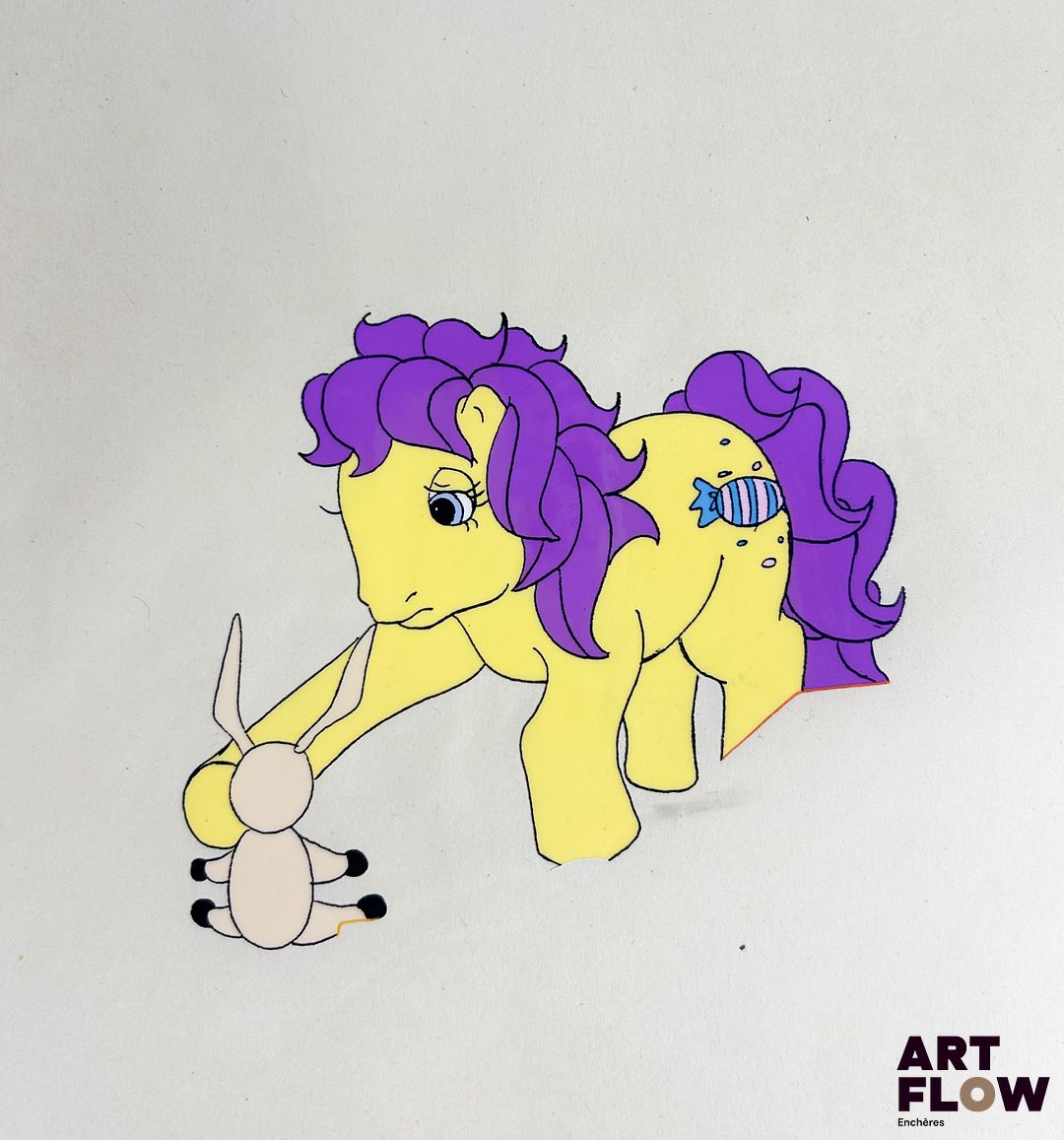 Mon Petit Poney (My Little Pony) Sweetie Drops Cellulo à l'encre et à la gouache représentant Sweetie Drops tenant un jouet Série d’animation et franchise américaine produite par Hasbro. « My Little Pony met en scène des poneys colorés évoluant dans un univers féerique où l’amitié, la solidarité et la bienveillance occupent une place centrale. Devenue une franchise emblématique depuis les années 1980, elle séduit par son esthétique vive, son univers enchanteur et ses messages positifs destinés à un large public. » Dimensions : 26,5 x 31,5 cm