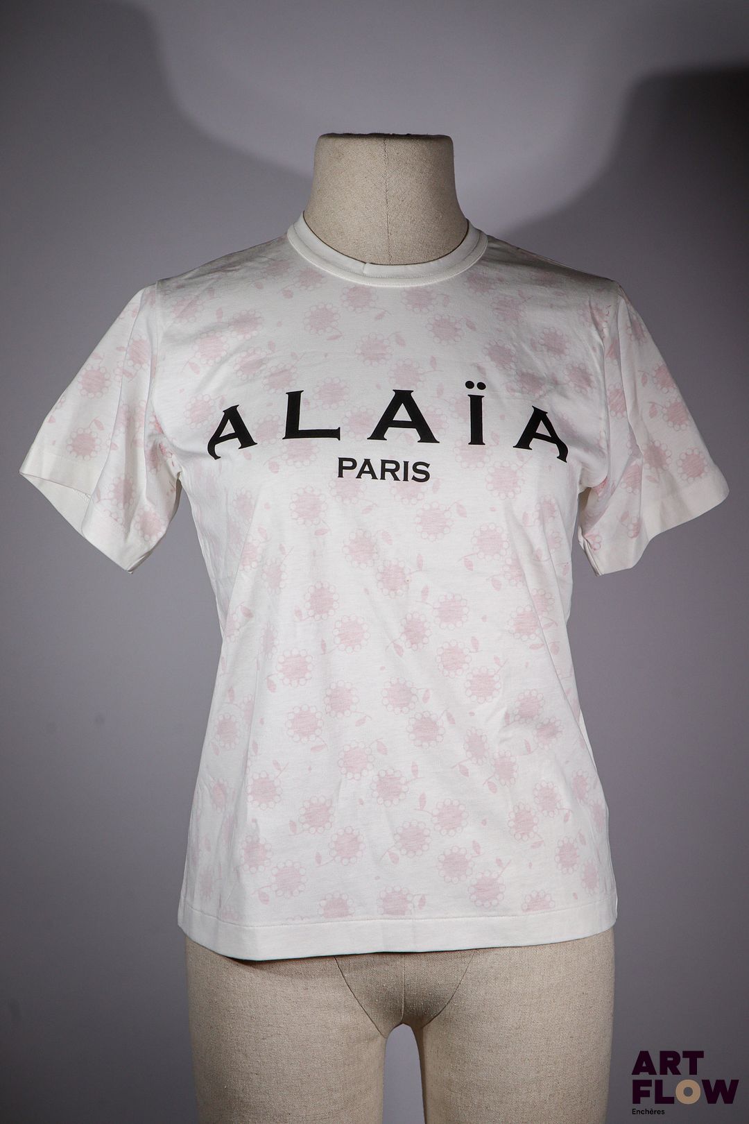 ALAIA Paris Tee shirt en coton blanc à motif de fleurs rouges imprimé du logo "ALAIA Paris" sur le devant. Taille présumée S/M. Très bon état général.