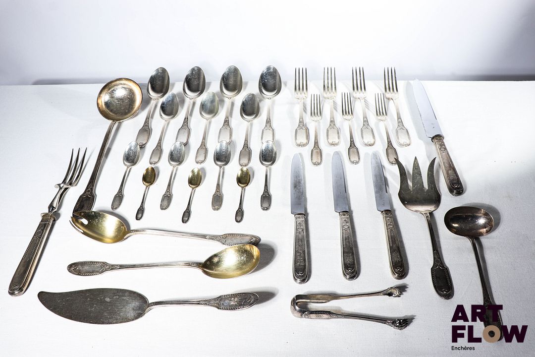 Partie de service de 93 pièces en argent massif à décor néoclassique comprenant : - 12 couverts de table (12 fourchettes et 12 cuillères) - 12 grands couteaux - 2 couverts à découpe - 1 louche - 1 cuillère à sauce - 2 couverts à salade en argent vermeillé - 12 petites fourchettes - 12 petites cuillères - 2 couverts de service à dessert - 12 cuillères à dessert - 1 pince à sucre - 12 cuillères à café en argent vermeillé Circa 1900 Poinçon Minerve 1er titre (950/1000) Chiffré MB Poids brut total : 5190,77 g Poids : 4410,1 g (sans les couteaux)