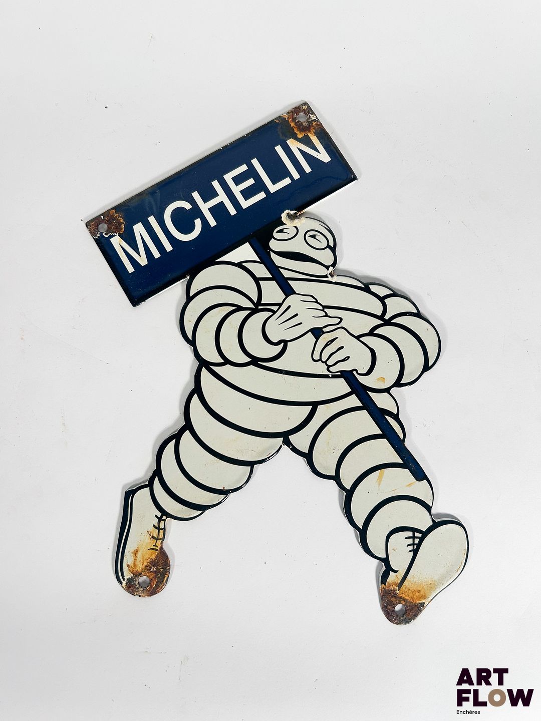 Plaque émaillée Michelin représentant le bonhomme Michelin portant une pancarte Dimensions : 28 x 22 cm Petits éclats et traces de rouille Reproduction moderne