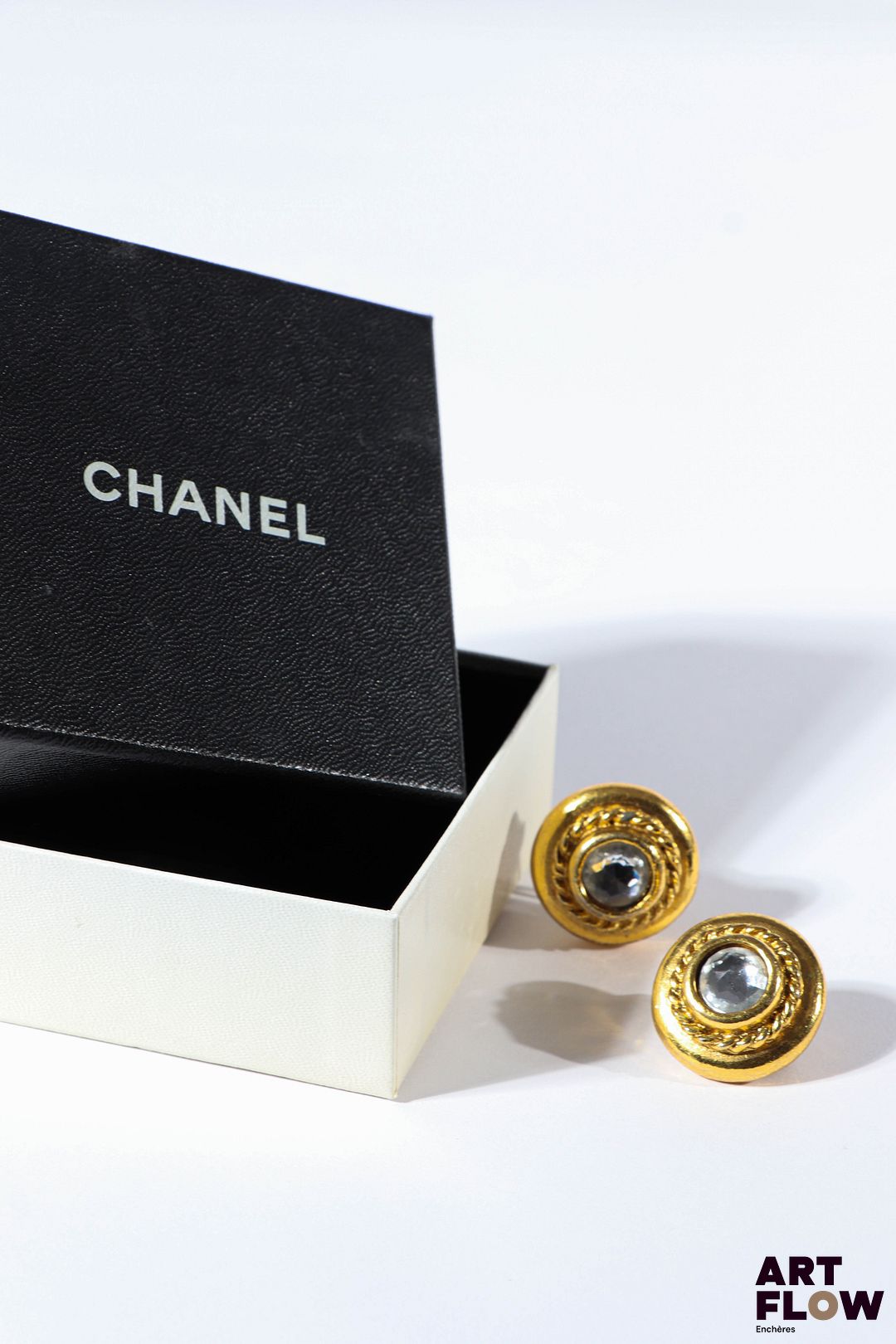 CHANEL Paire de clips d'oreilles en métal doré de forme ronde centrée chacune d'un strass. Diamètre : 2,5 cm environ Dans leur boîte d'origine.