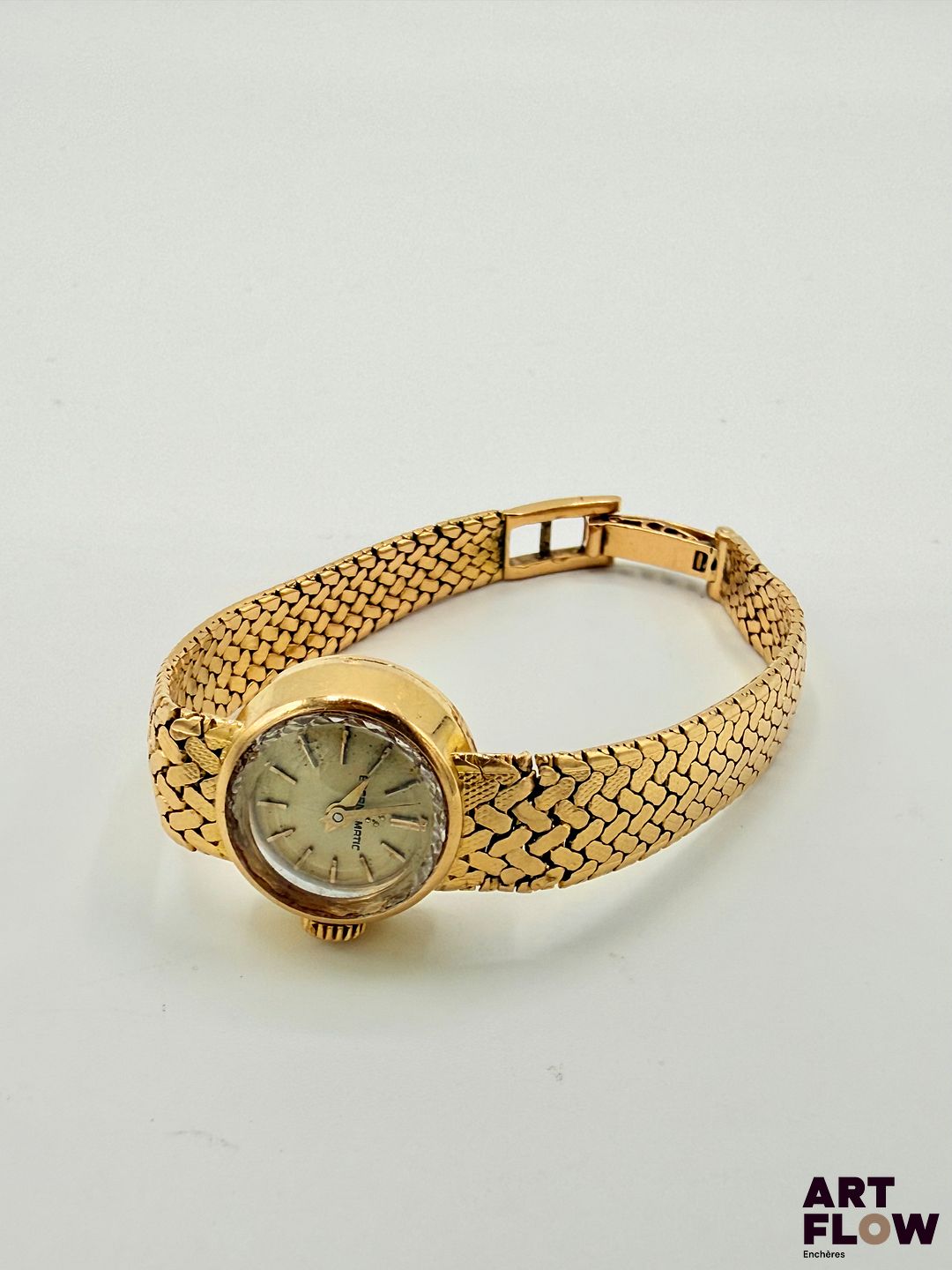 ETERNA Montre bracelet de dame en or 750/°°, à mouvement mécanique à remontage automatique, masse oscillante en or, le boîtier rond à cadran à fond champagne, index bâtons, aiguilles dauphine Poinçon Paul Franck et fils Diamètre 16 mm Longueur du bracelet : 14,5 cm env. Poids brut : 31,86 gr Bon état général (maillons endommagés) Fonctionnelle au moment de la rédaction du catalogue, mécanisme non garanti. La marque Eterna est une maison horlogère suisse fondée en 1856, reconnue pour ses innovations techniques, notamment l’introduction du rotor à roulement à billes en 1948, qui a révolutionné les montres automatiques. Elle s’est aussi illustrée avec la collection KonTiki, inspirée d’une célèbre expédition maritime. Aujourd’hui, Eterna reste associée à la précision suisse et à un riche héritage horloger. Le poinçon de maître permet également d’en apprendre davantage sur cette pièce. En effet, la manufacture Paul Franck était spécialisée dans la fabrication de boîtiers en métaux précieux à Taverny. Dans les années 1960, les villes de Taverny et de Saint-Leu-la-Forêt constituaient le principal centre de fabrication de boîtiers de montres de la région parisienne.