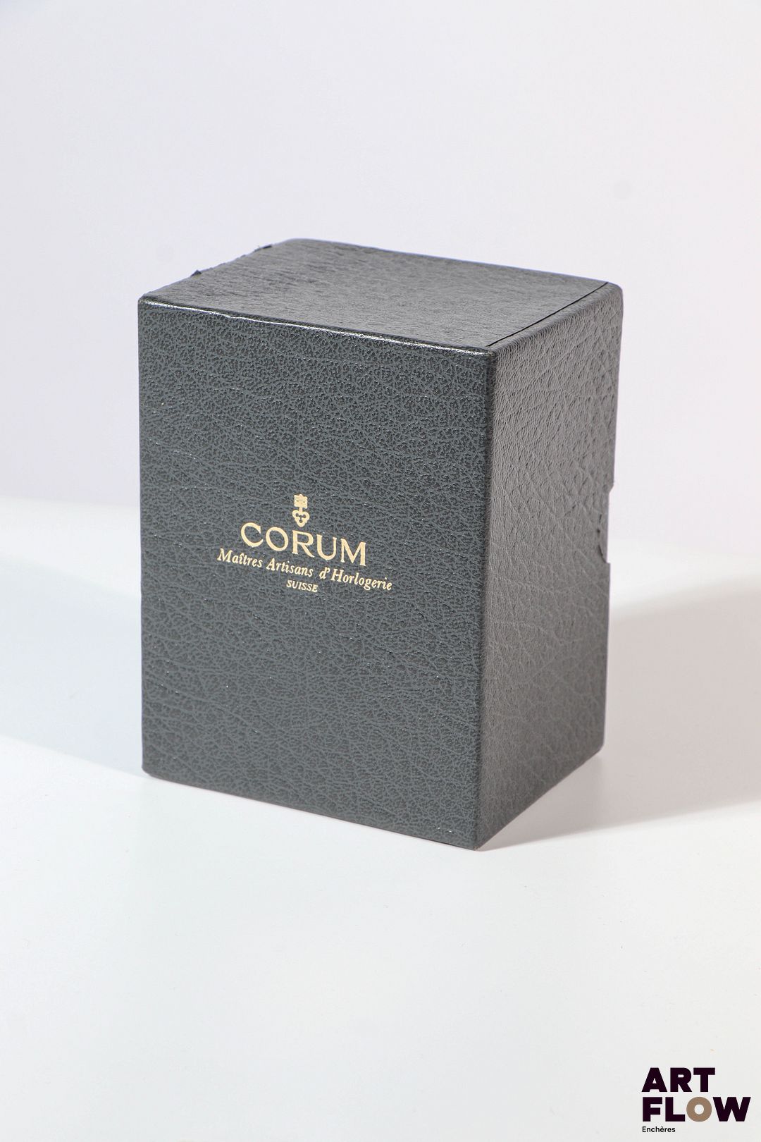 CORUM Boite en cuir gris et sur boite en carton grise Emblème de la marque sur la boite en métal doré 12 x 8,5 x 7 cm pour la boîte Traces d'usage, bon état général