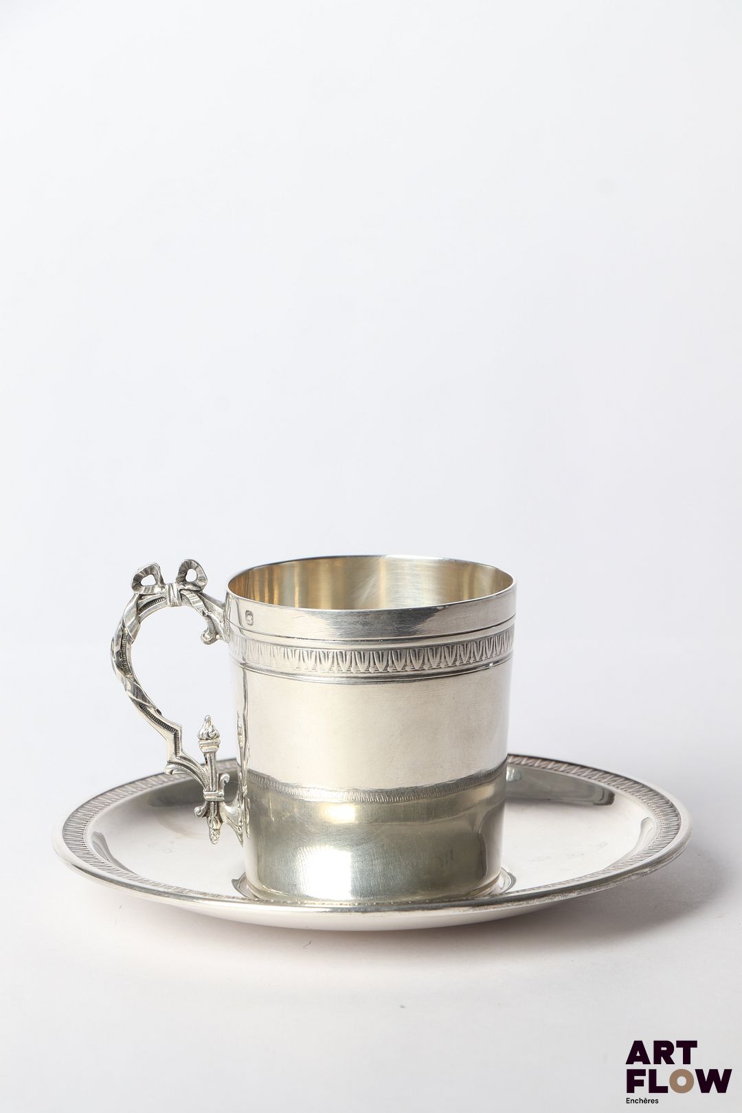 Tasse et sous tasse en argent (poinçon Minerve) de style néo-classique à décor de frises de feuilles d'eau, l'anse de la tasse ornée d'un noeud. Poinçon de maître Henri Gauthier, 1902/1920, 29 rue Beaubourg, Paris Poids total : 177,21 gr